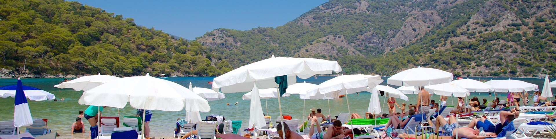 A crowded beach with white umbrellas and people sunbathing.