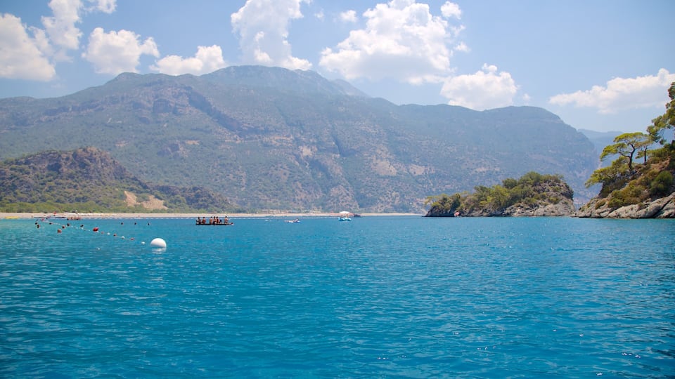 A coastal scene with clear blue water, boats, and a mountainous backdrop.
