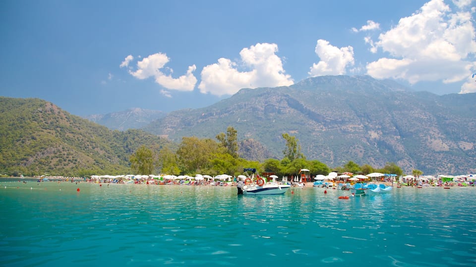 A turquoise lake with boats, umbrellas, and people. Mountains and trees are in the background.