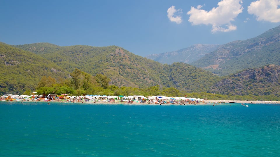 A beach with clear turquoise water, umbrellas, and people.
