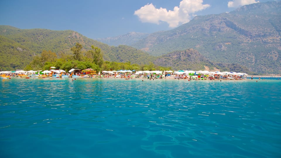 A beach with clear blue water, umbrellas, and people.