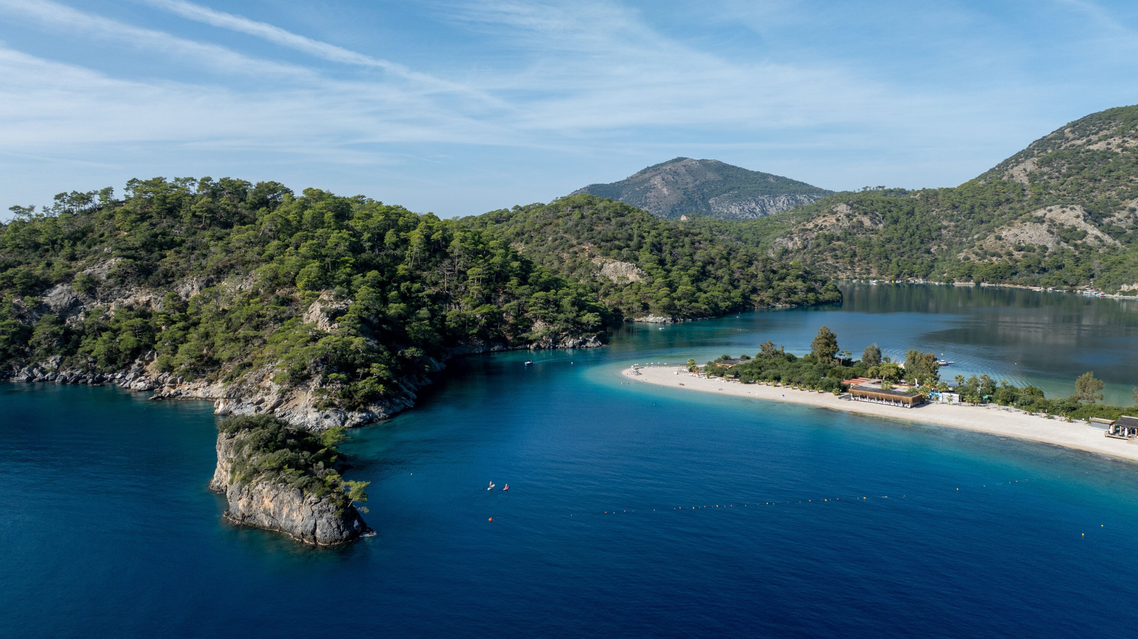 A coastal landscape with a small island, clear blue waters, and surrounding hills.