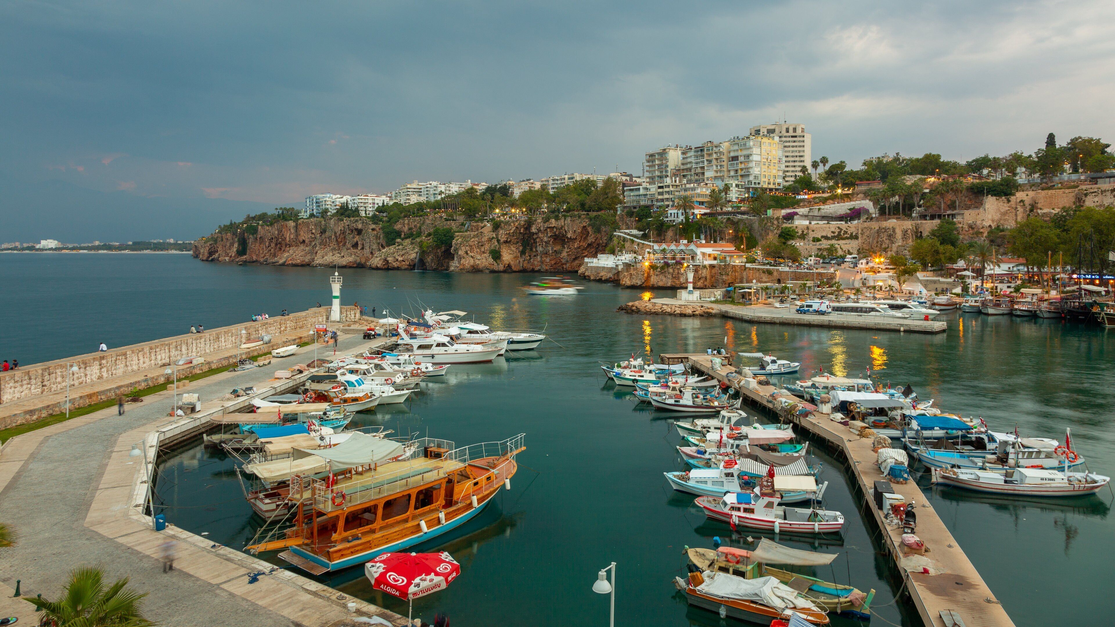 A marina with various boats docked, a lighthouse, and buildings on a hillside.