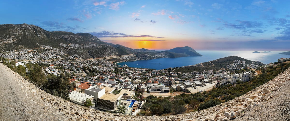 A coastal town with a view of the sea, mountains, and a sunset.