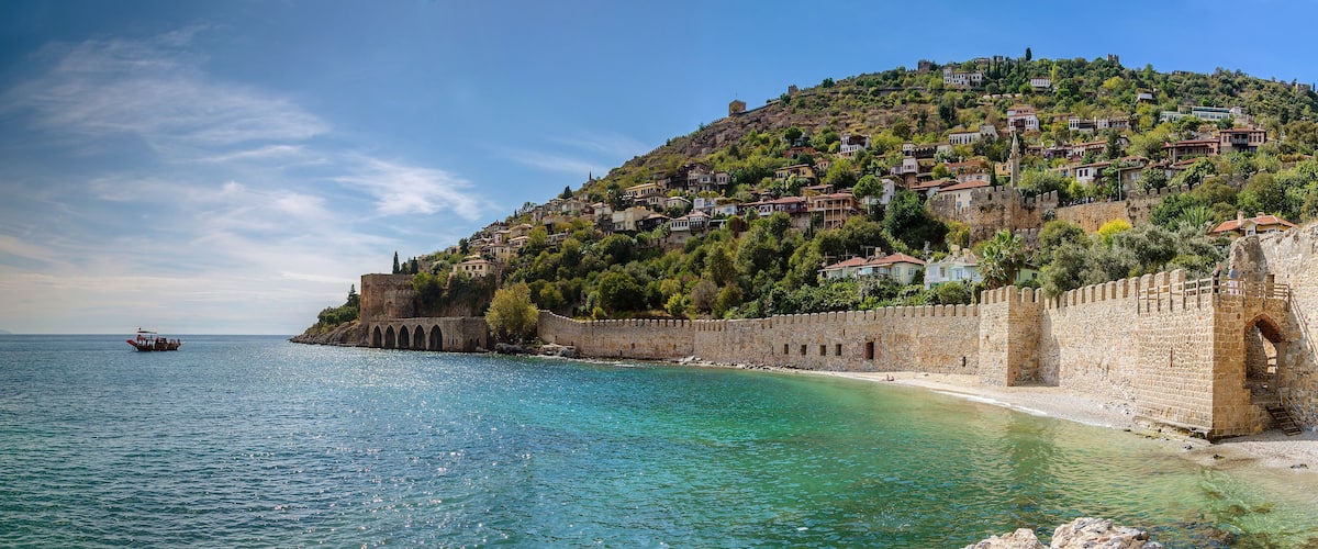 A coastal town with a historic stone wall, clear turquoise waters, and a boat on the sea.