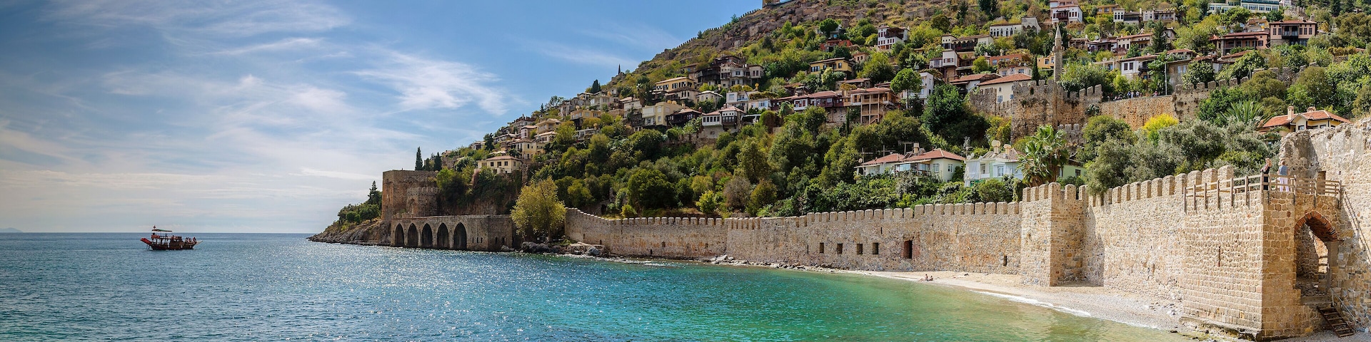 A coastal town with a historic stone wall, clear turquoise waters, and a boat on the sea.