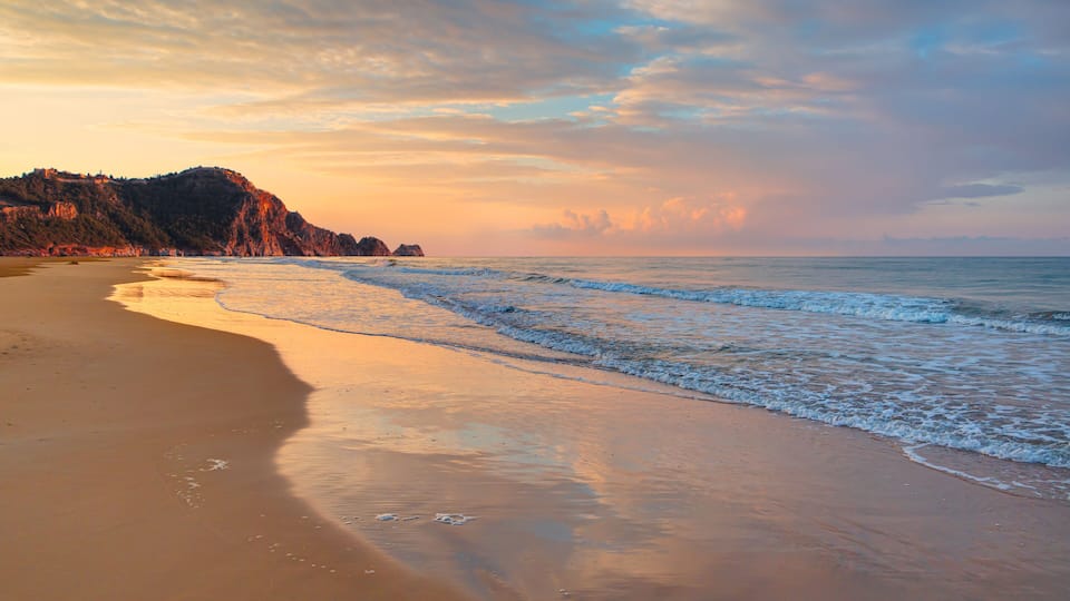 A beach with waves, a cliff, and a sunset sky.