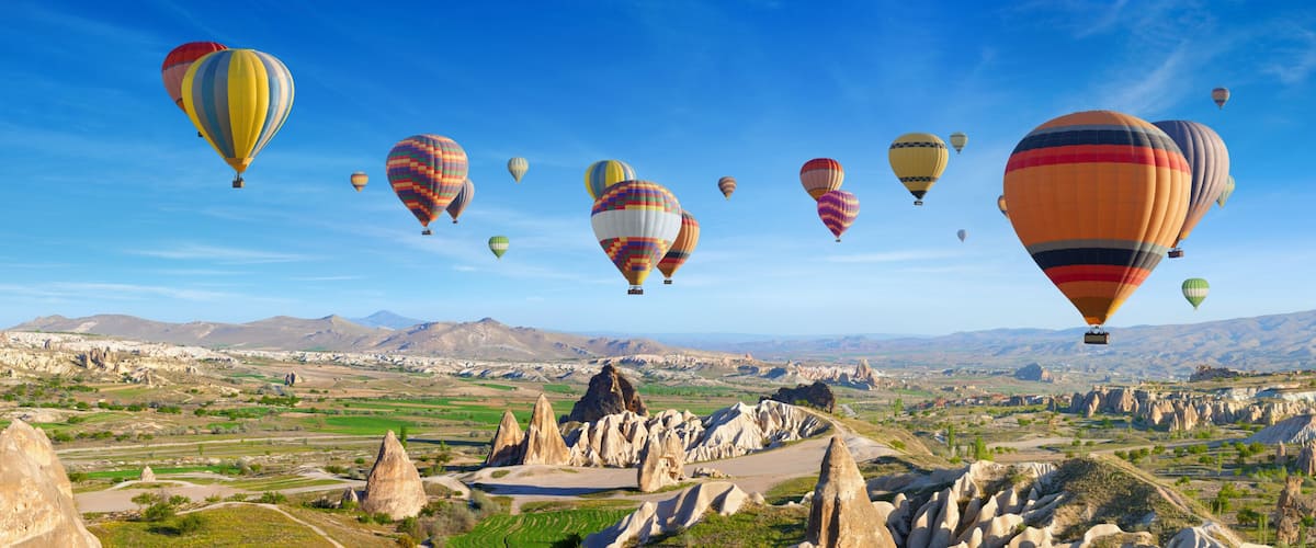 A landscape with numerous hot air balloons, rugged terrain, and distant mountains.
