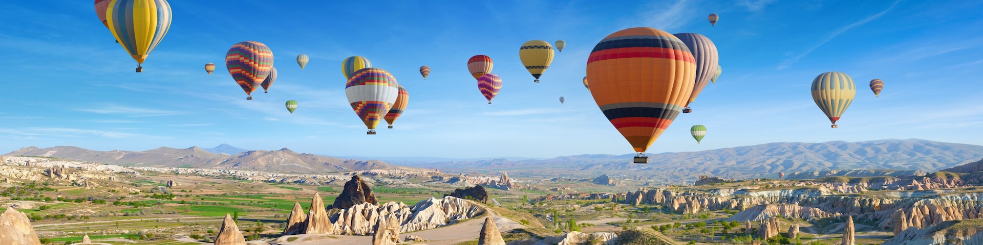 Un paysage parsemé de nombreux ballons à air chaud, avec un terrain accidenté et des montagnes à l’horizon.