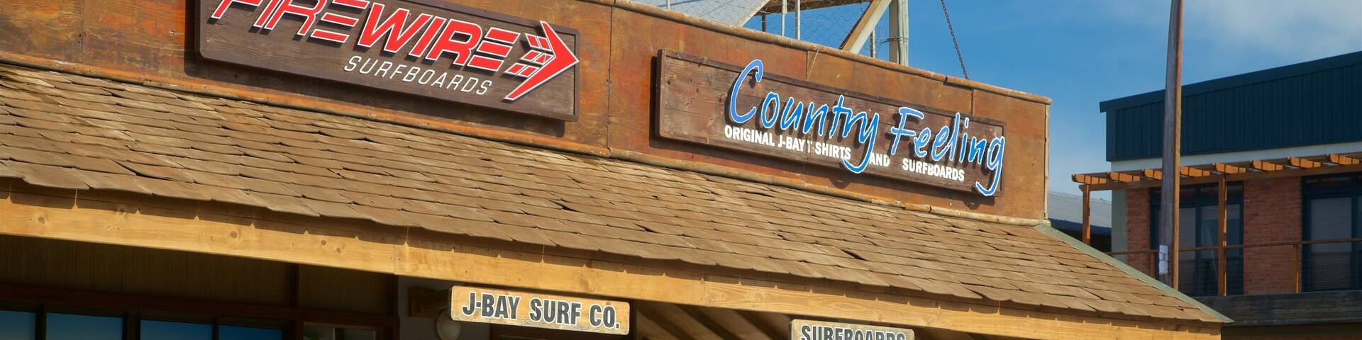 A surf shop with signs for 'FREWIRE SURFBOARDS' and 'Country Feeling Original J-Bay T-Shirts and Surfboards'.