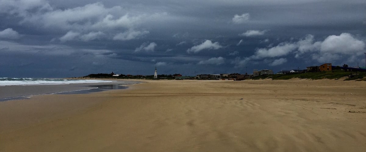A beach with a cloudy sky and a distant lighthouse.