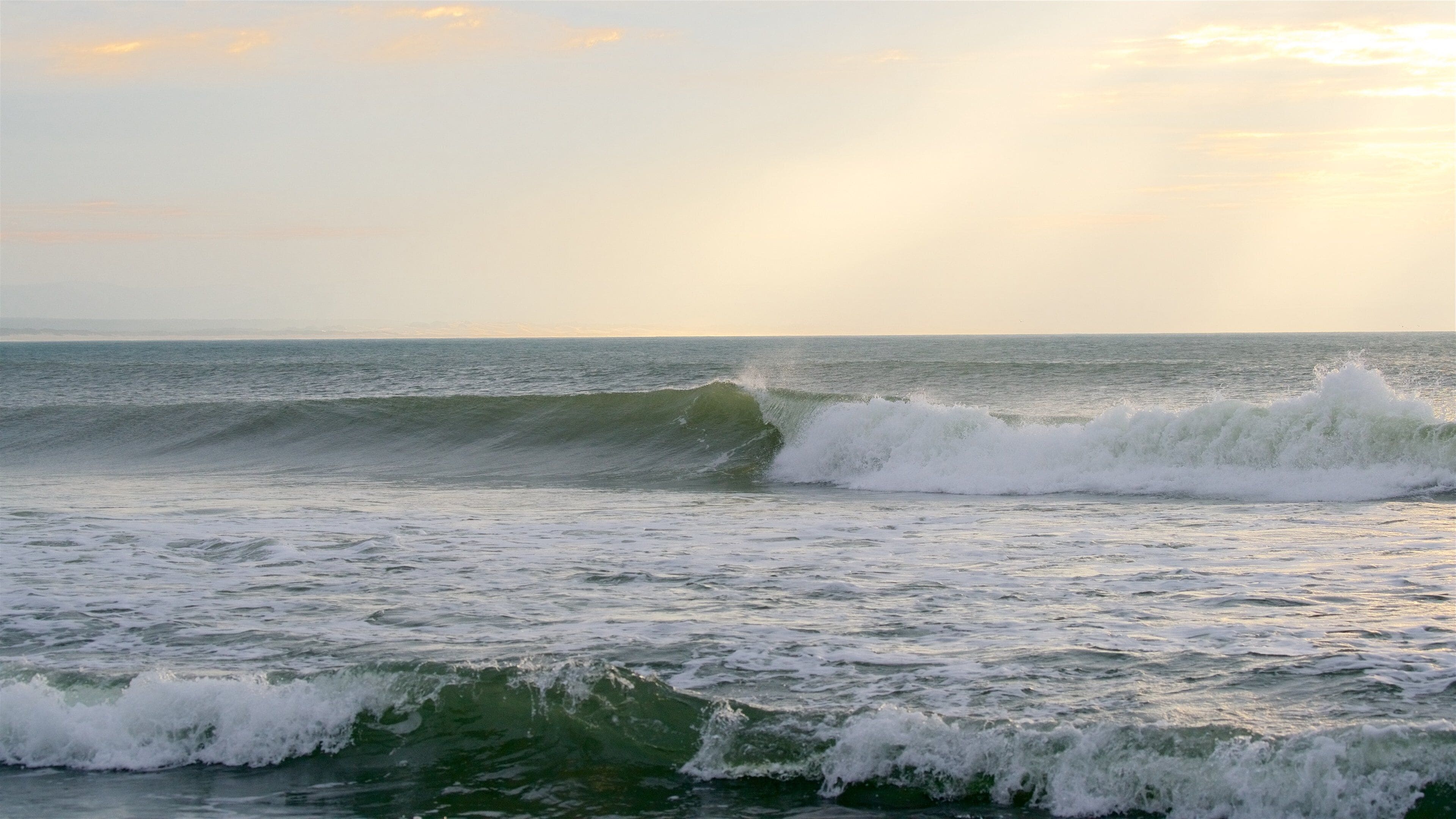 A beach with waves and a sunset.