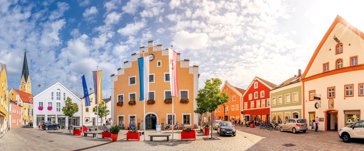 A cobblestone square with colorful buildings, a church spire, and flags.
