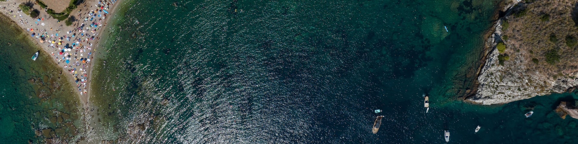 An aerial view of a coastal area with a beach, a swimming pool, and a densely packed row of umbrellas.