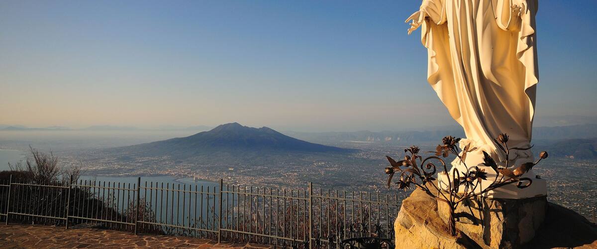 A statue of a robed figure overlooking a cityscape with a mountain in the background.