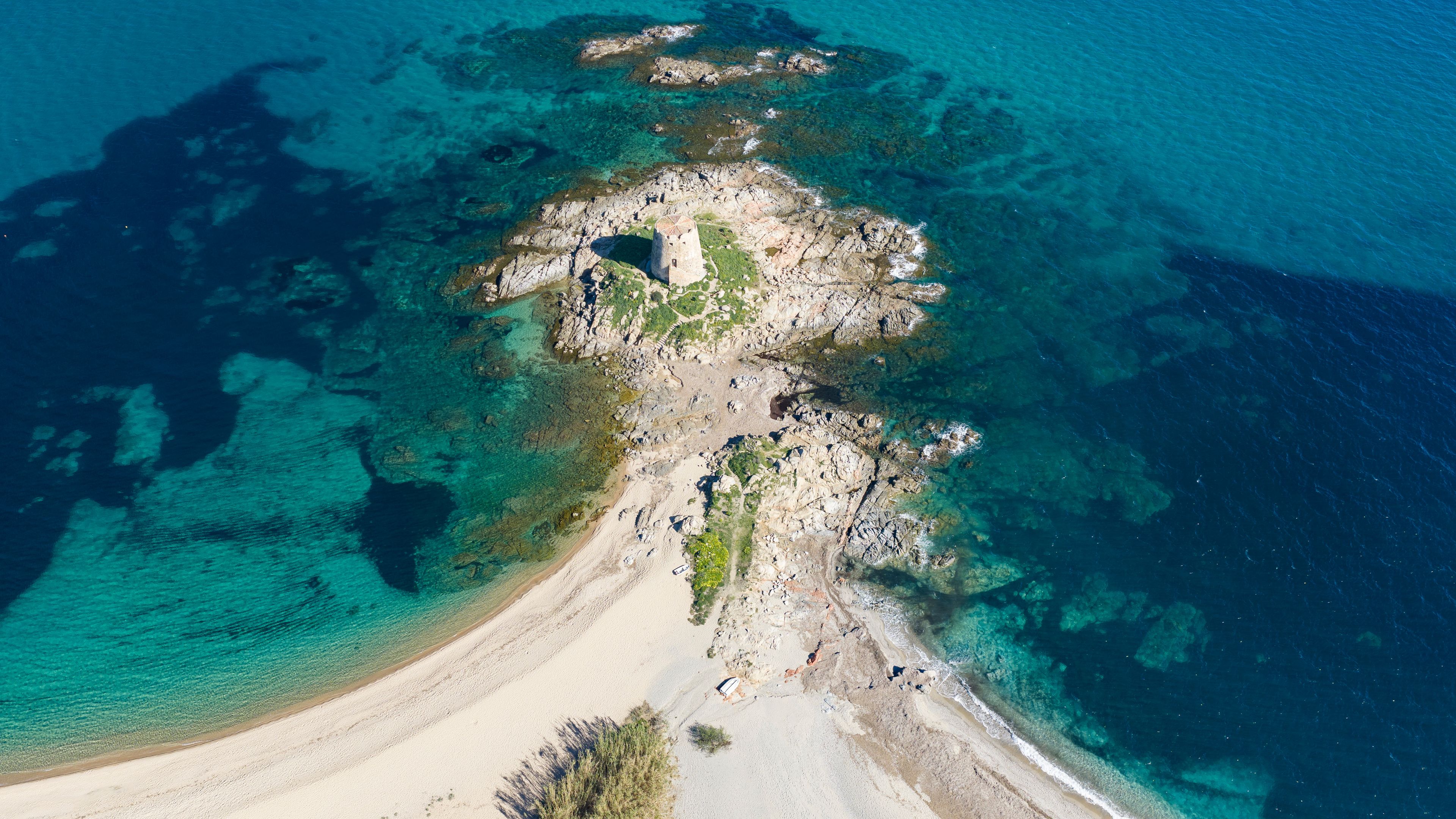 Aerial view of Torre di Bari, medieval Spanish watchtower on a rocky islet connected by sandy beach in Bari Sardo, Sardinia, Italy. Turquoise sea and crystal clear water in summer.