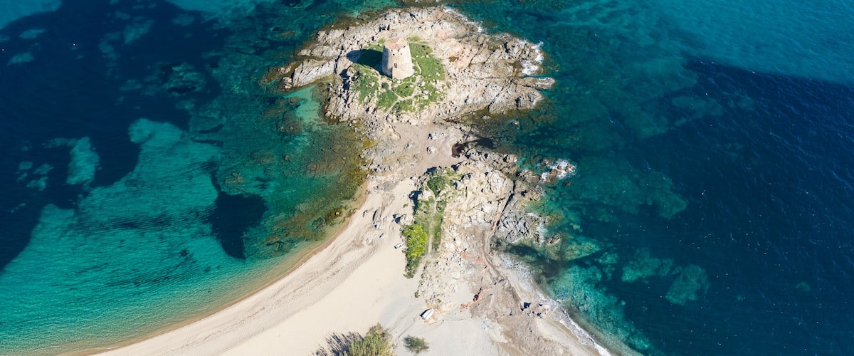 Aerial view of Torre di Bari, medieval Spanish watchtower on a rocky islet connected by sandy beach in Bari Sardo, Sardinia, Italy. Turquoise sea and crystal clear water in summer.