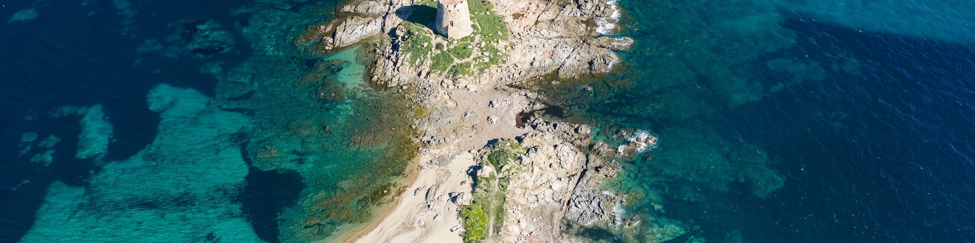 Aerial view of Torre di Bari, medieval Spanish watchtower on a rocky islet connected by sandy beach in Bari Sardo, Sardinia, Italy. Turquoise sea and crystal clear water in summer.