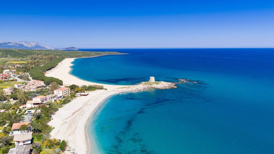 A coastal landscape with a sandy beach, clear blue waters, and a small island with a tower.