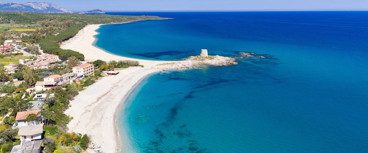 A coastal landscape with a sandy beach, clear blue waters, and a small island with a tower.