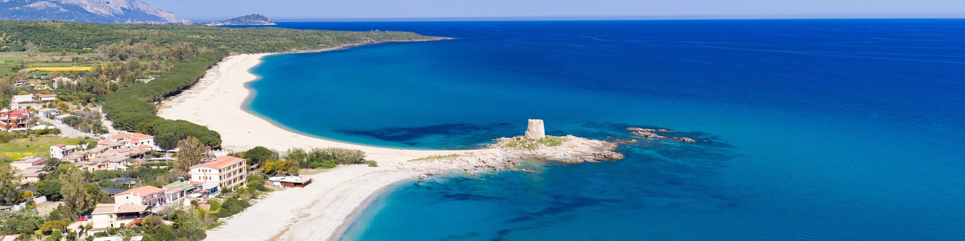 A coastal landscape with a sandy beach, clear blue waters, and a small island with a tower.