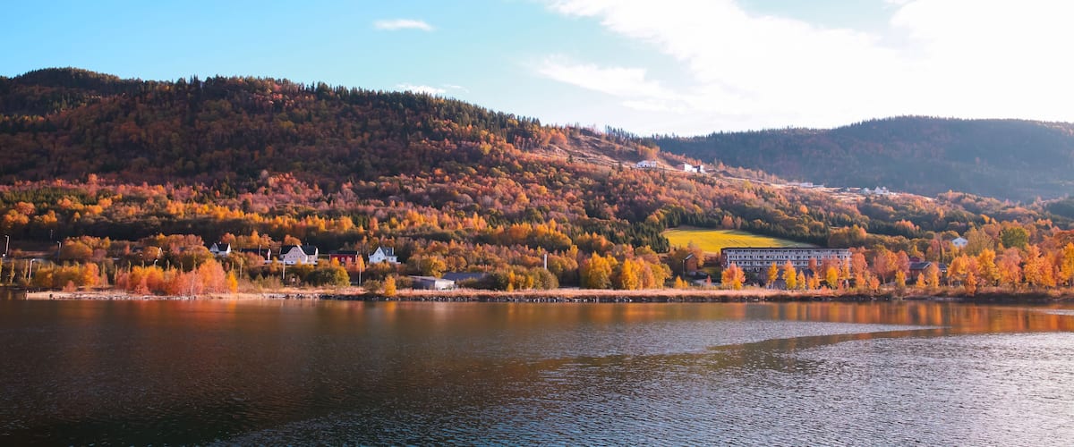 A lake with autumn-colored trees, a bridge, and buildings on a hillside.