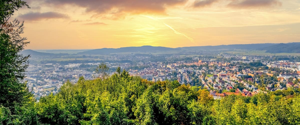 A cityscape with a sunset, surrounded by dense green forests.
