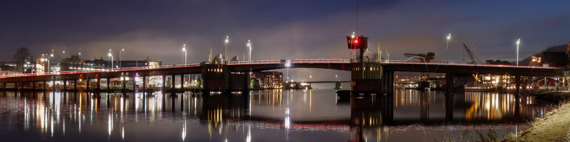 A nighttime river bridge with illuminated lights reflecting on the water.