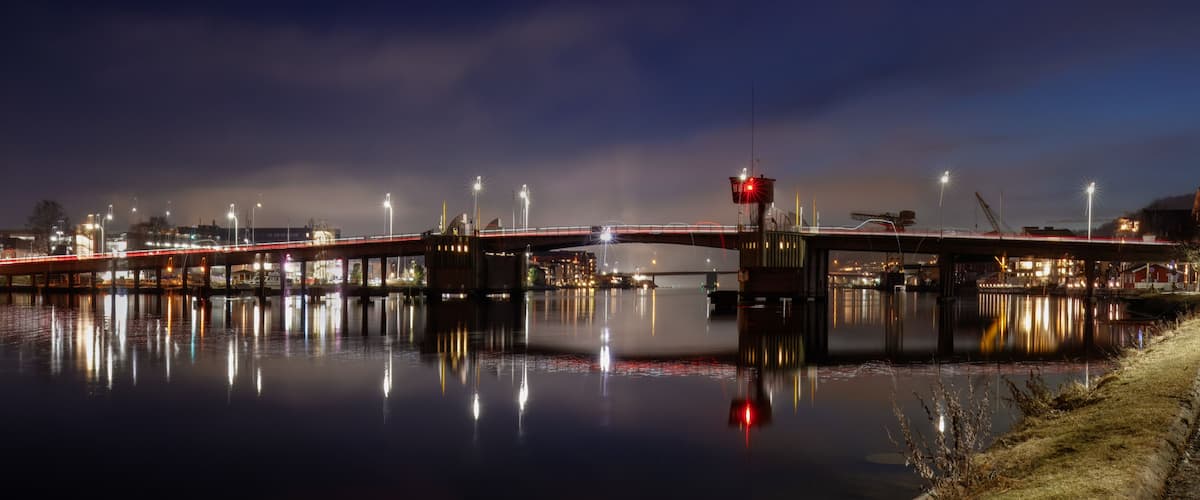 A nighttime river bridge with illuminated lights reflecting on the water.