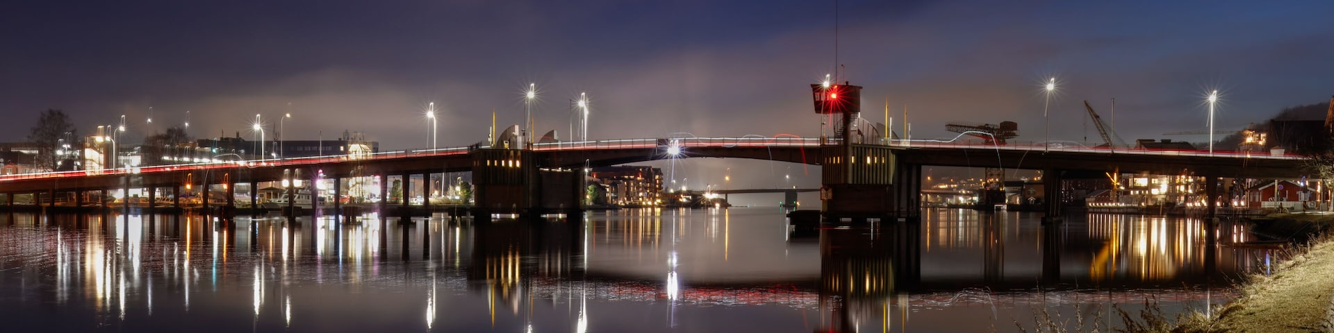 A nighttime river bridge with illuminated lights reflecting on the water.