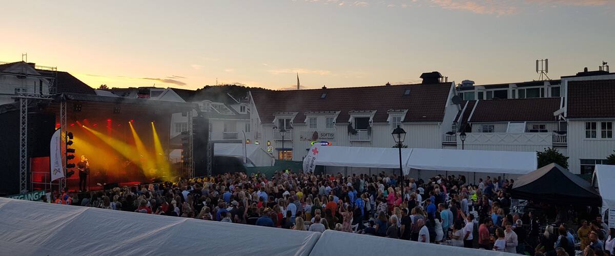 A crowded outdoor event with a stage and audience at sunset.