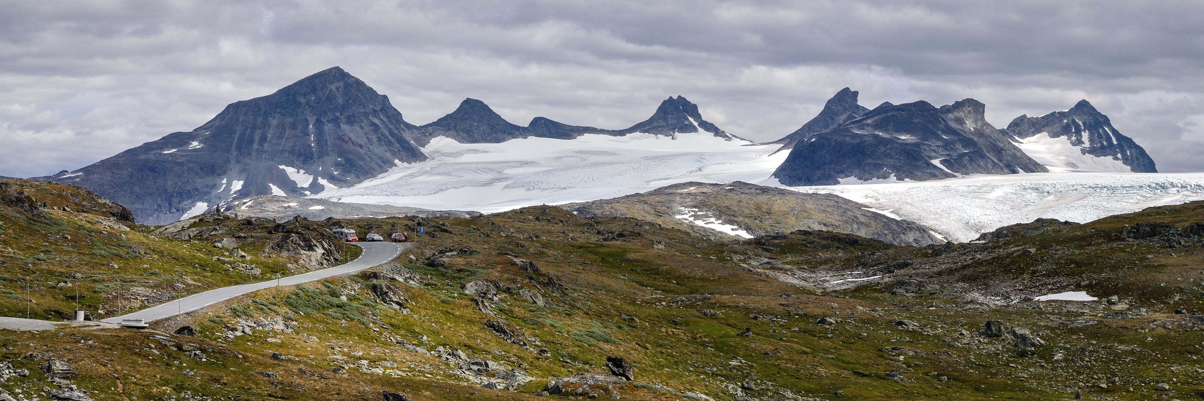 A winding mountain road with snow-capped peaks in the background.