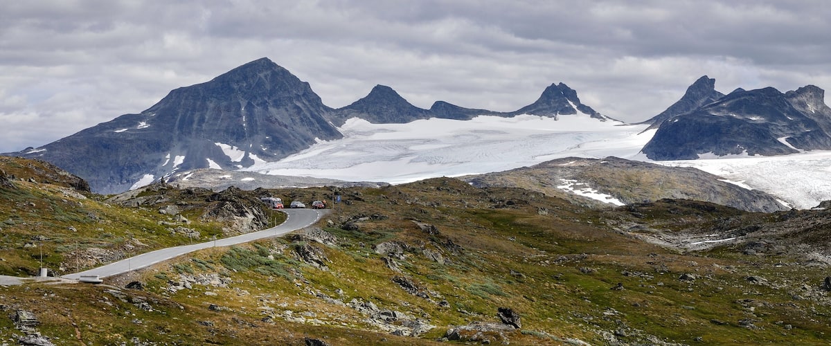 A winding mountain road with snow-capped peaks in the background.