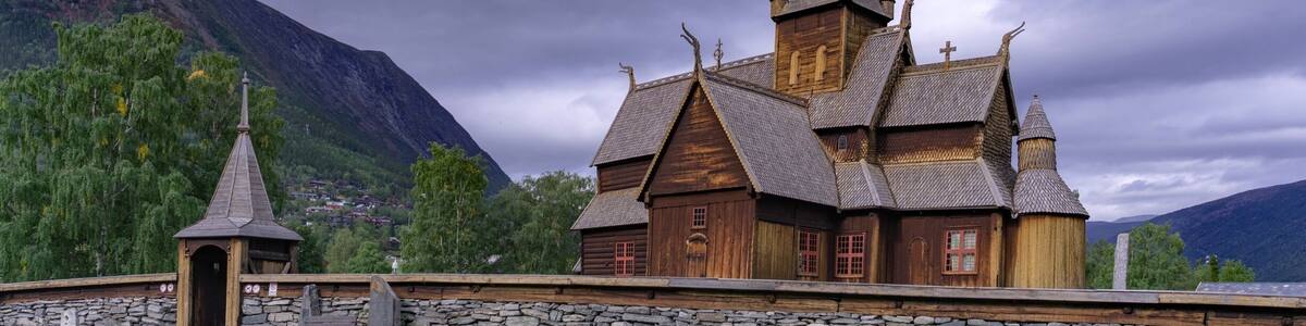A wooden church with a tall spire, set against a mountainous backdrop.