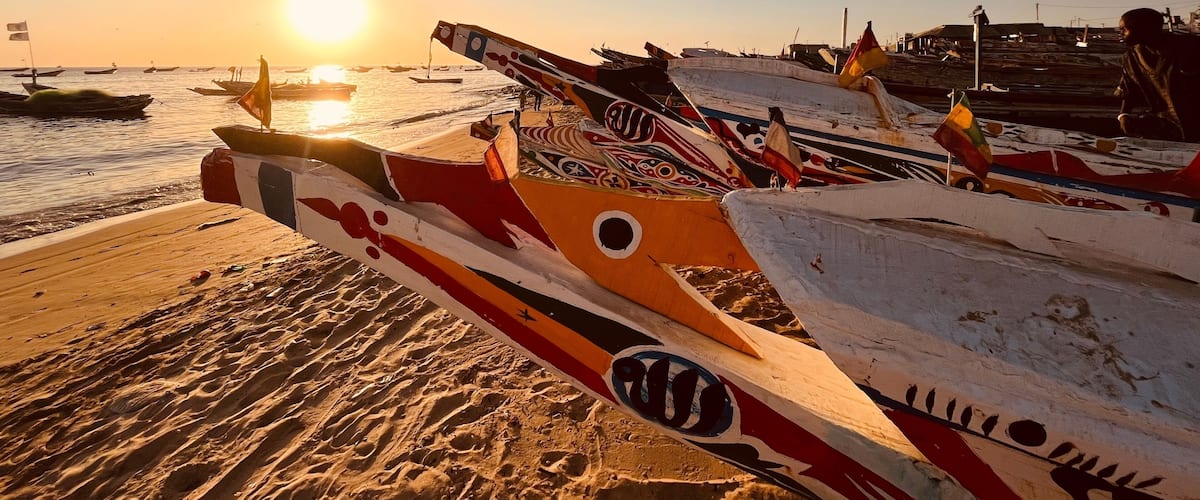 A beach with several colorful boats docked, the sun setting in the background.