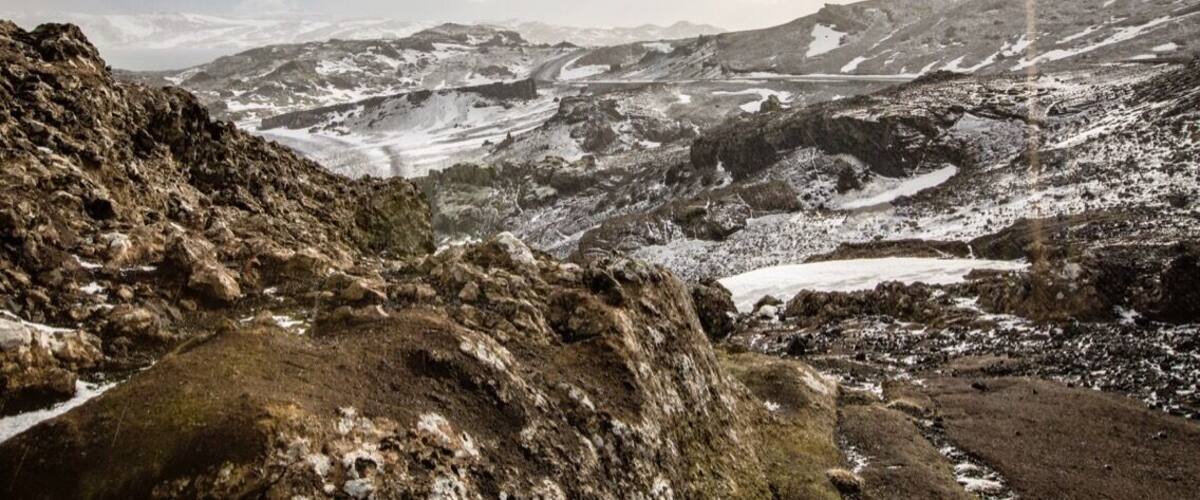 A rugged mountainous landscape with snow patches and a winding path.