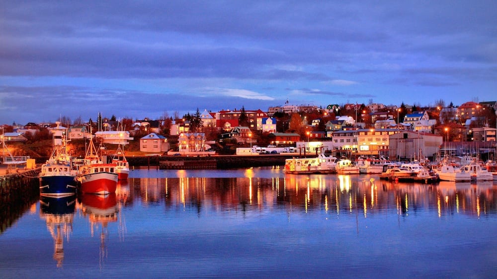 A harbor at dusk with boats docked and buildings in the background.