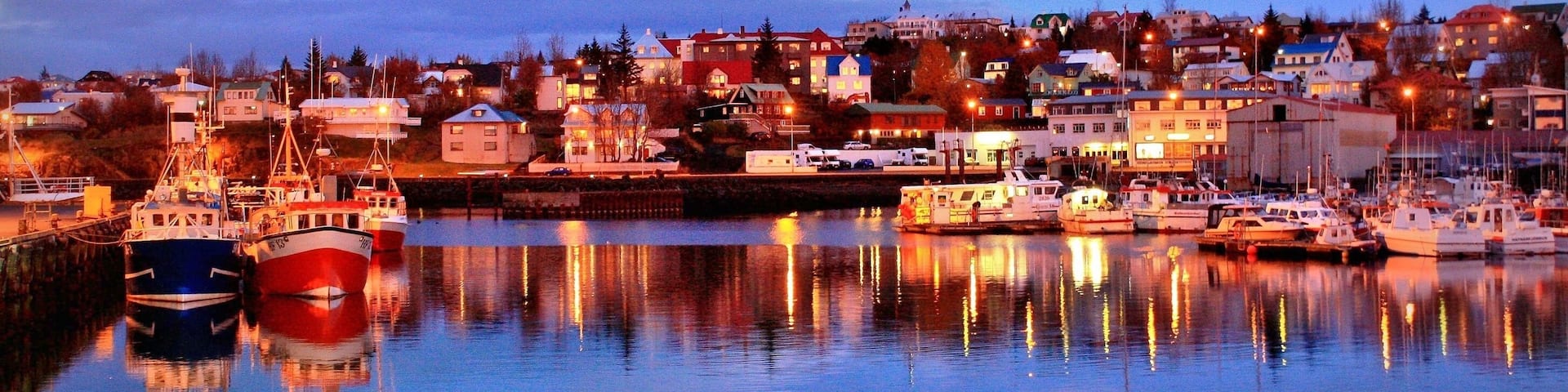 A harbor at dusk with boats docked and buildings in the background.