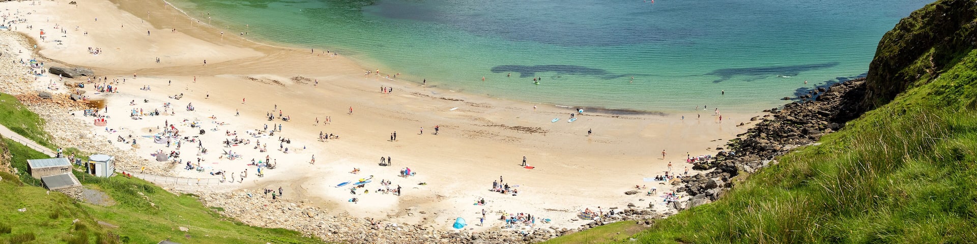 Panorama image of Keem bay beach on a warm sunny day. Achill island, county Mayo, Ireland, Irish landscape. Tourists on the beach, Blue cloudy sky. Beautiful blue ocean color