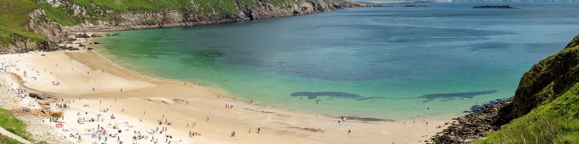 Panorama image of Keem bay beach on a warm sunny day. Achill island, county Mayo, Ireland, Irish landscape. Tourists on the beach, Blue cloudy sky. Beautiful blue ocean color