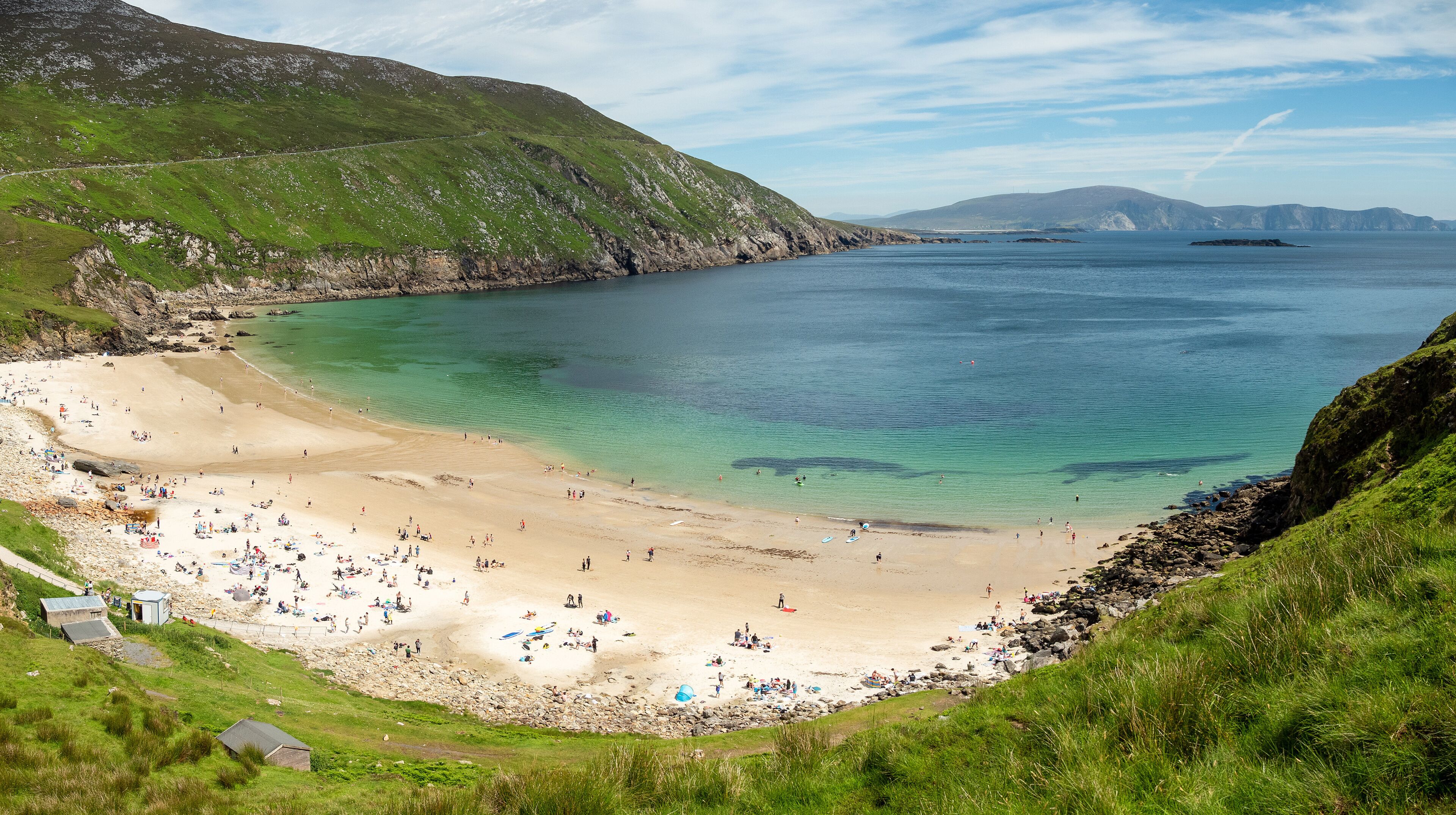 A coastal landscape with a sandy beach, rocky cliffs, and a clear blue sea.