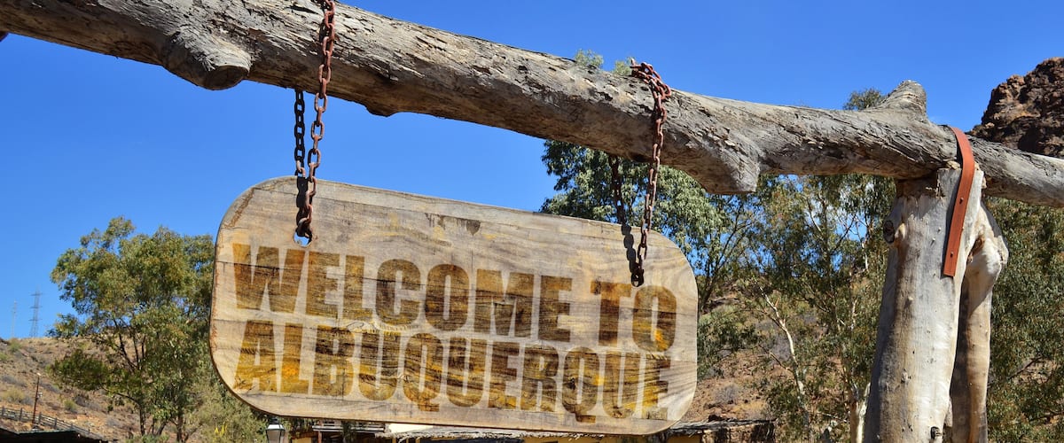 A wooden sign reading "WELCOME TO ALBUQUERQUE" hanging from a tree.