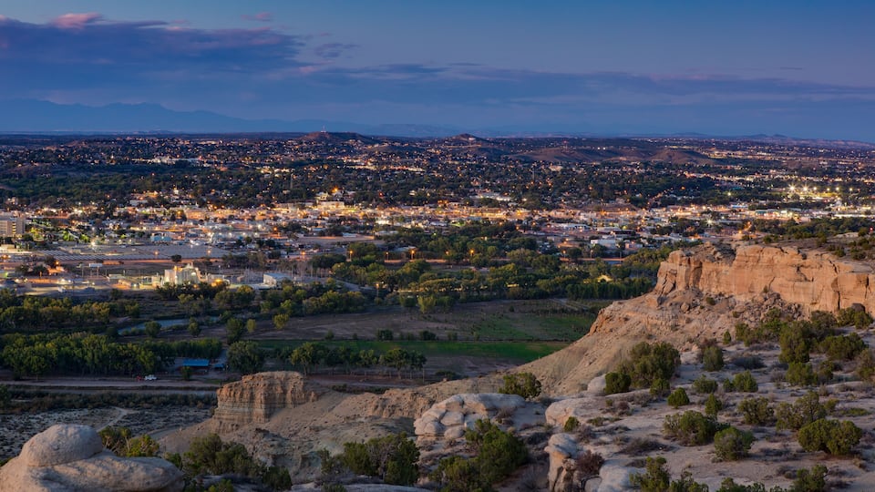 A cityscape at dusk with a prominent rocky outcrop in the foreground.