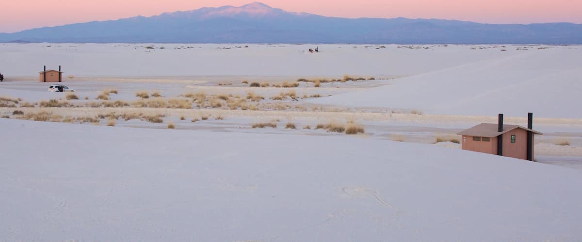 A snowy landscape with a small building and a distant mountain range.