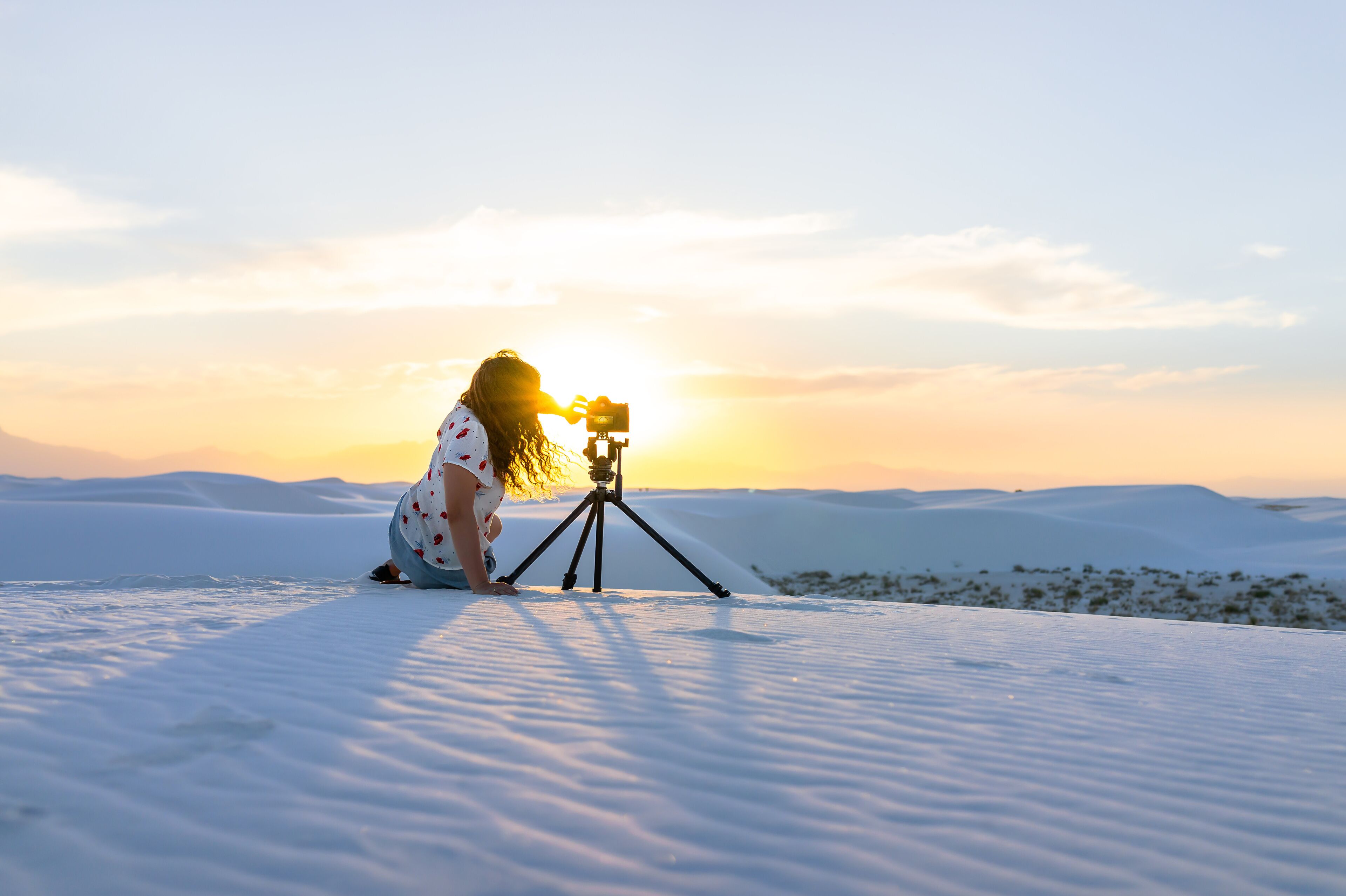 A person with a camera on a tripod on a snowy landscape during sunset.