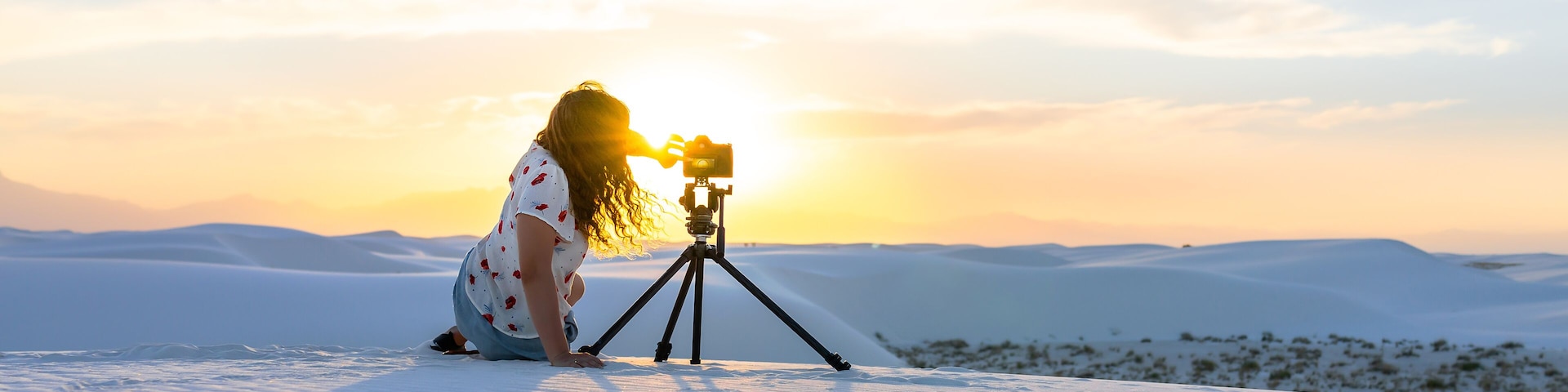 A person with a camera on a tripod on a snowy landscape during sunset.