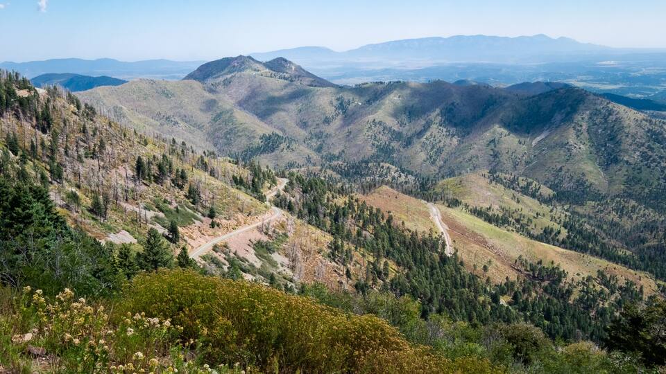 A mountainous landscape with winding roads and dense forests.