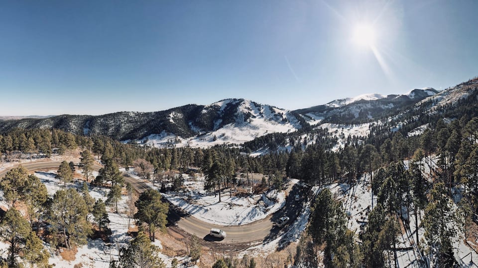 A snow-covered mountainous landscape with a winding road and dense forests.
