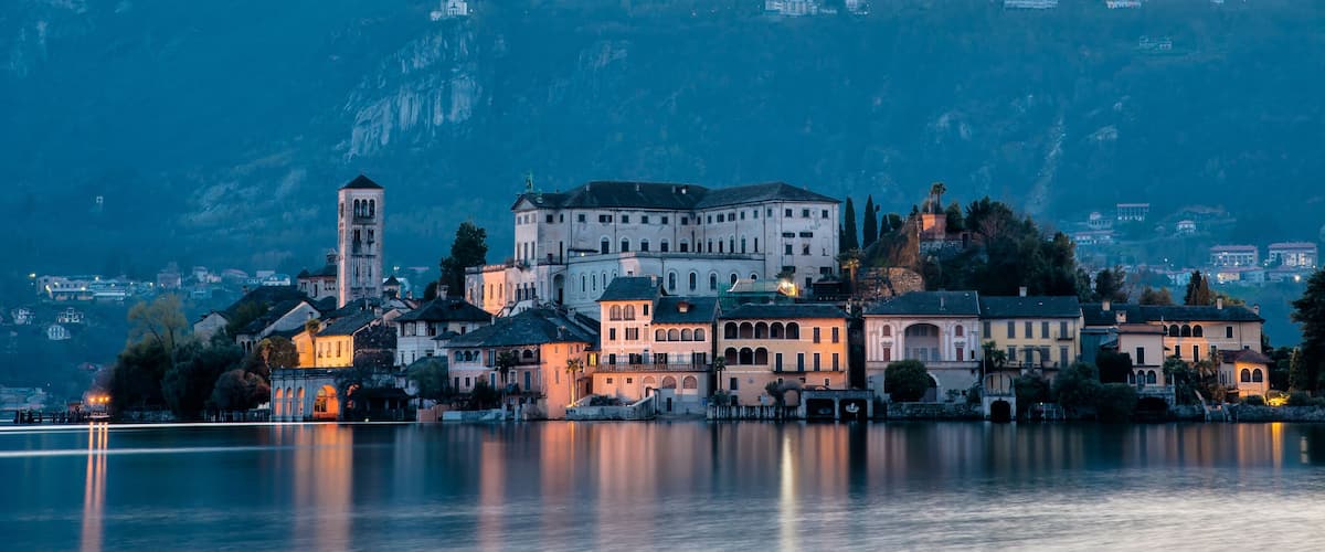 A historic lakeside town with a prominent castle and tower, surrounded by mountains and calm water.
