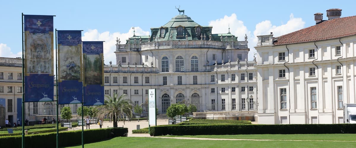 A large, ornate building with a green dome and white facade, surrounded by well-manicured lawns and a clear blue sky.